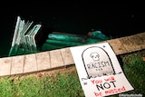 A statue is partially submerged in a pond, with a sign reading "racism, you will not be missed" next to it.