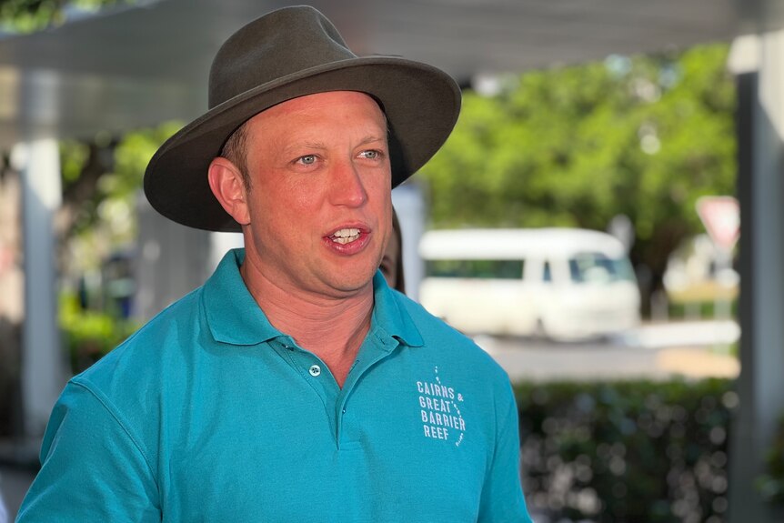 A man wearing a teal polo and a brown hat speaking to media