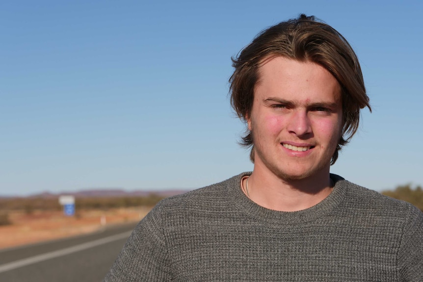 Cullen Shoesmith is standing by the road, wearing a jumper and smiling at the camera.