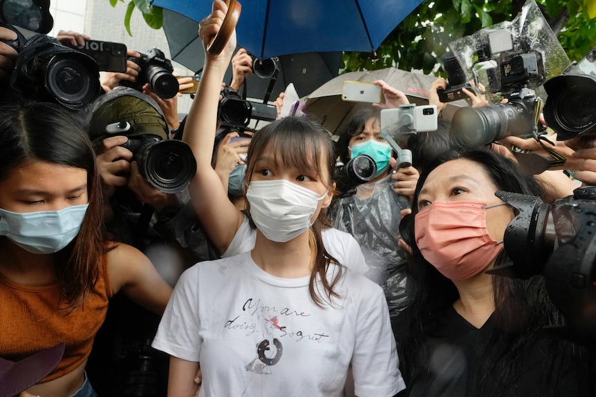 Agnes Chow wearing a mask leaves prison surrounded by a crowd of media. 