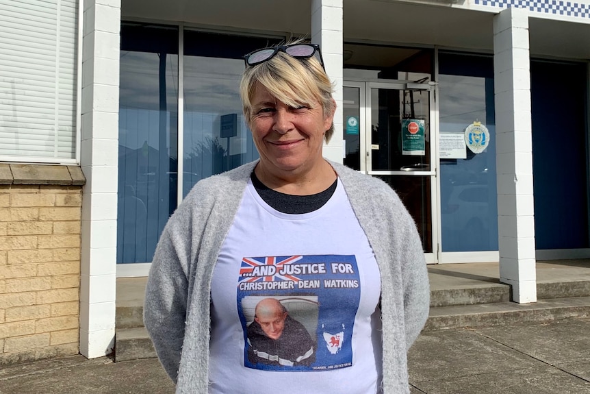 A woman stands outside a police station wearing a shirt with a picture of her missing son on it. He's suspected murdered