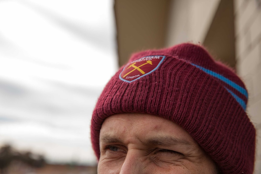 A close up on squinting eyes beneath a maroon beanie with a logo that reads 'London'.