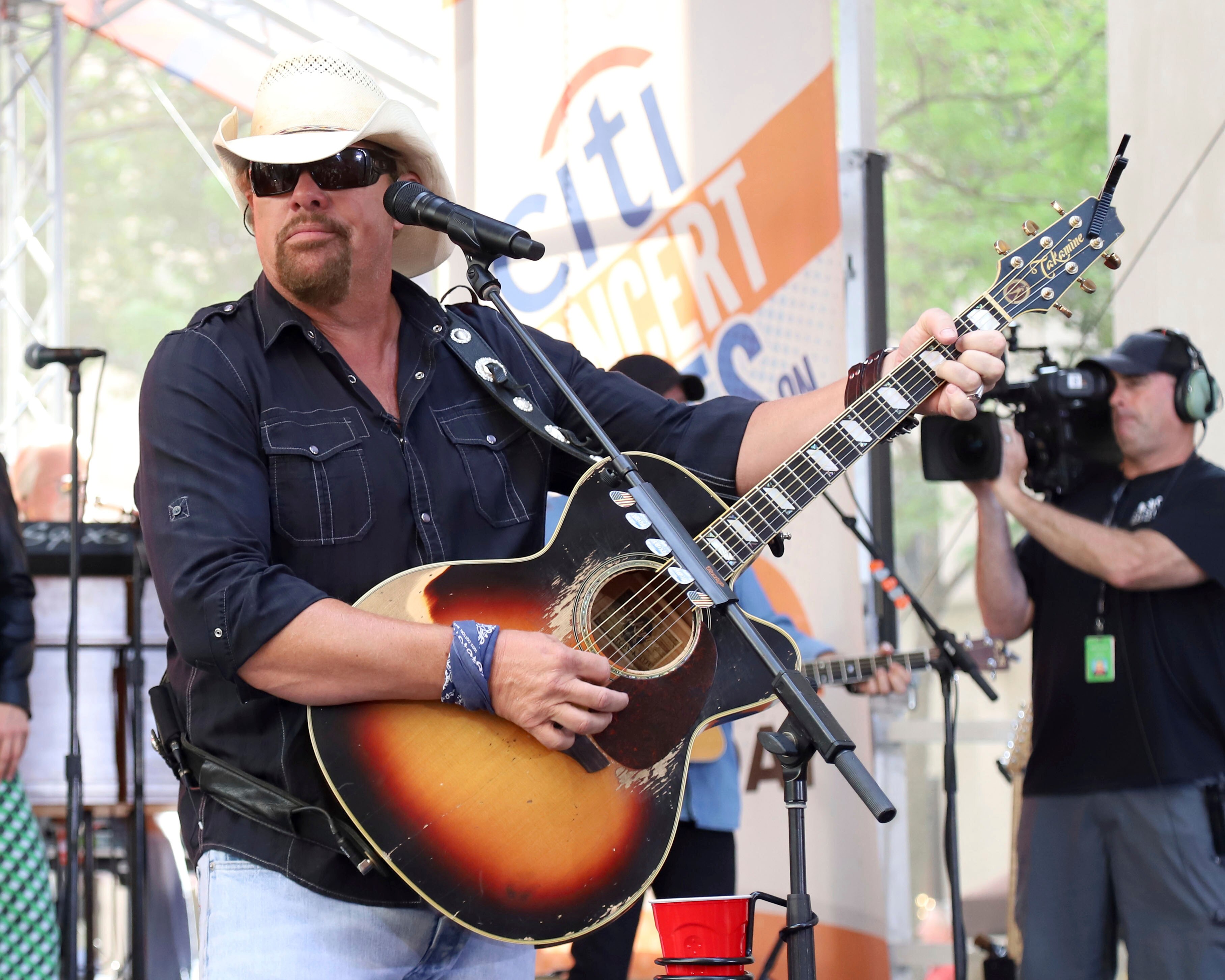 A man wearing a cowboy hat and sunglasses strums his guitar.