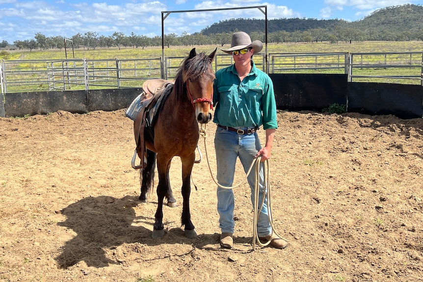 A man standing in a horse yard with a tan horse.