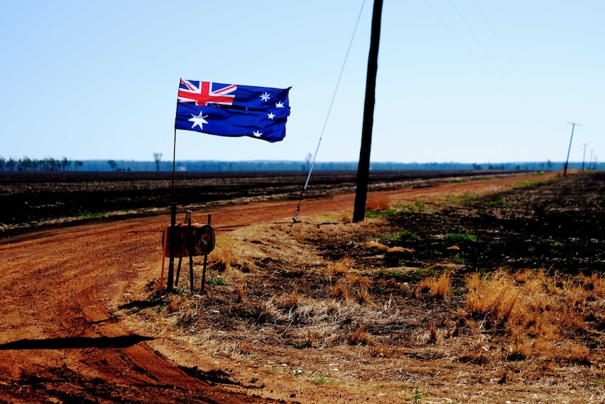 An Australian flag flutters in the wind in a dry landscape in country Australia.