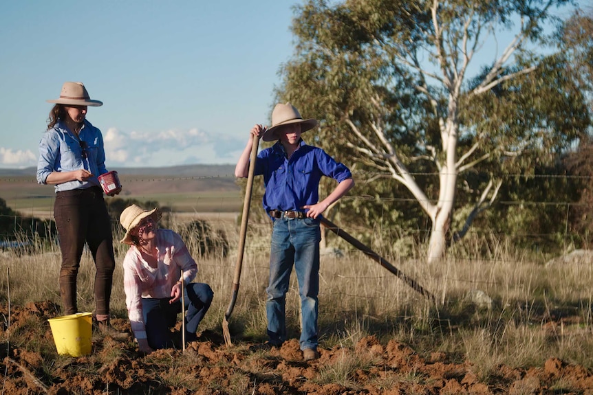 A teenage boy and two woman stand by a barbed wire fence on a rural property