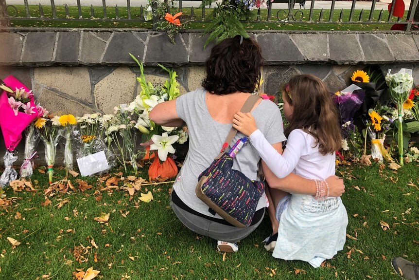 Rear shot of woman and small girl laying flowers at memorial with arms around each other.