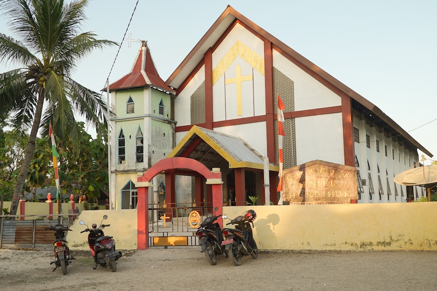 Sebuah gereja menara putih dengan sepeda motor duduk di depan gerbang.