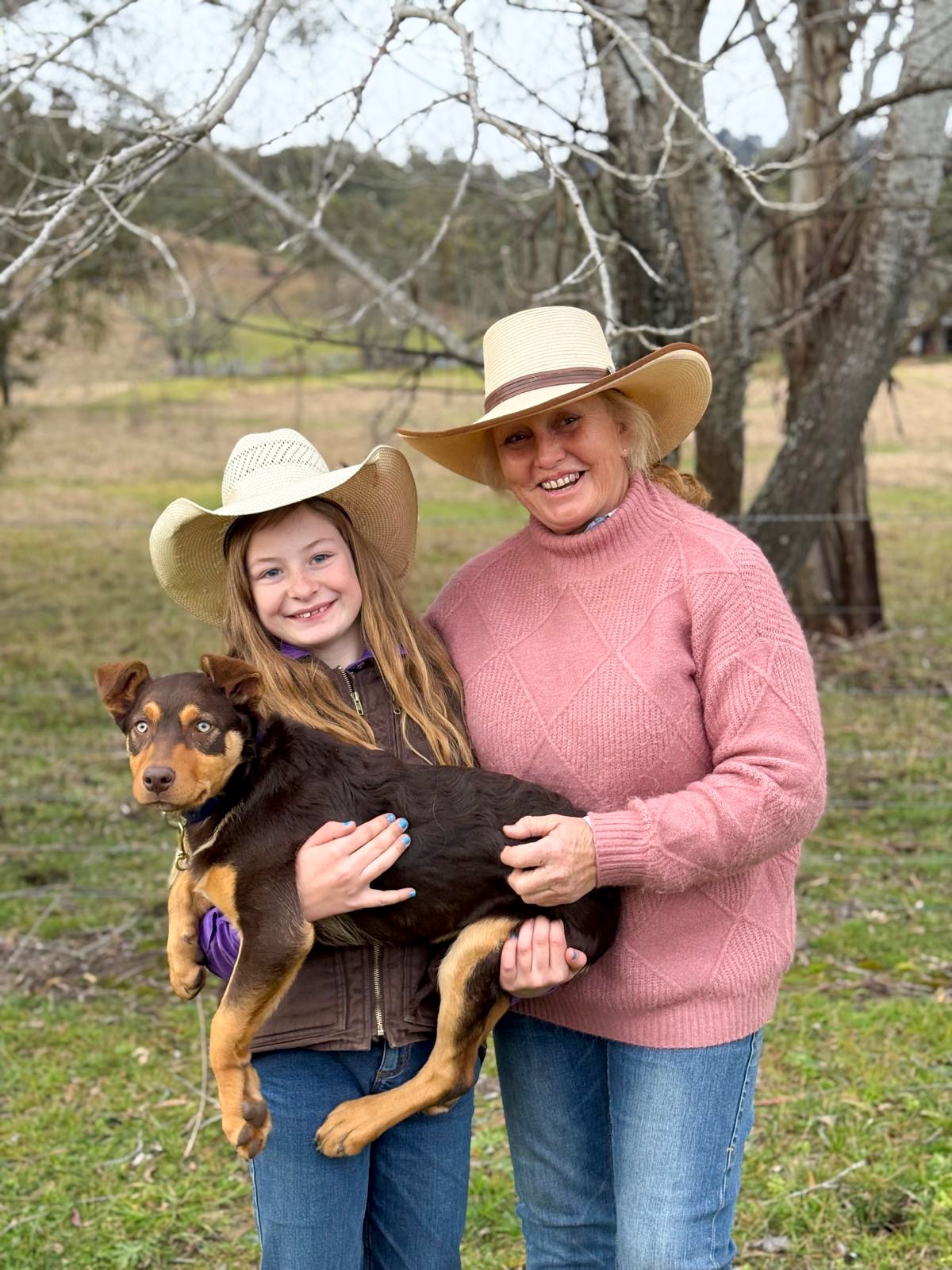 Una niña está de pie con una mujer sosteniendo su cachorro Kelpie.