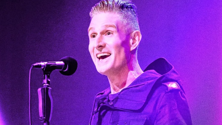 man smiling behind microphone in pink light