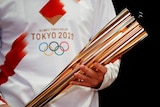 A person in a white t-shirt bearing the Tokyo Olympics logo holding the golden Olympic torch