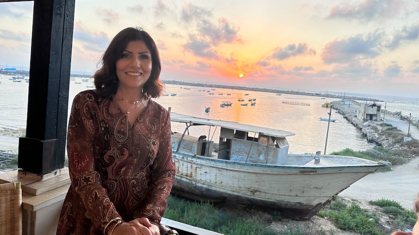 Samah Sabwai stands on a balcony at sunset in front of a boat.