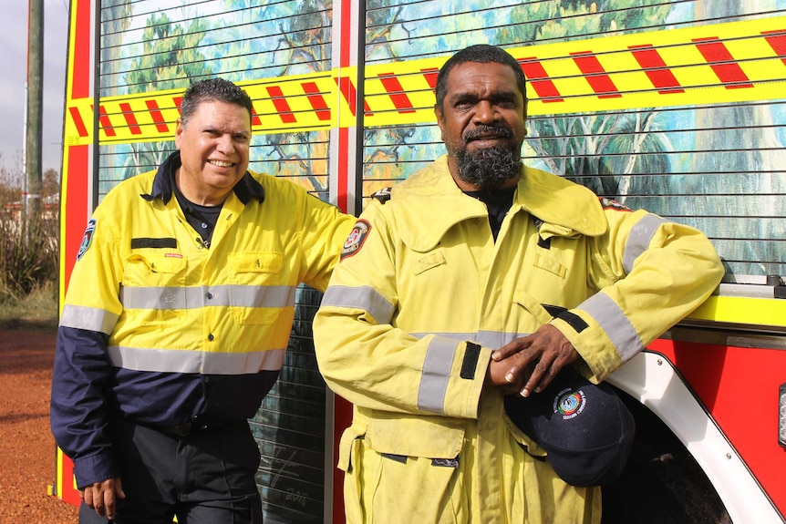Two fire officers in high viz standing in front of fire truck with Aboriginal painting on it.