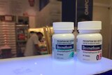 Two medicine bottles that read dexamethasone sit on the bend of a pharmacy