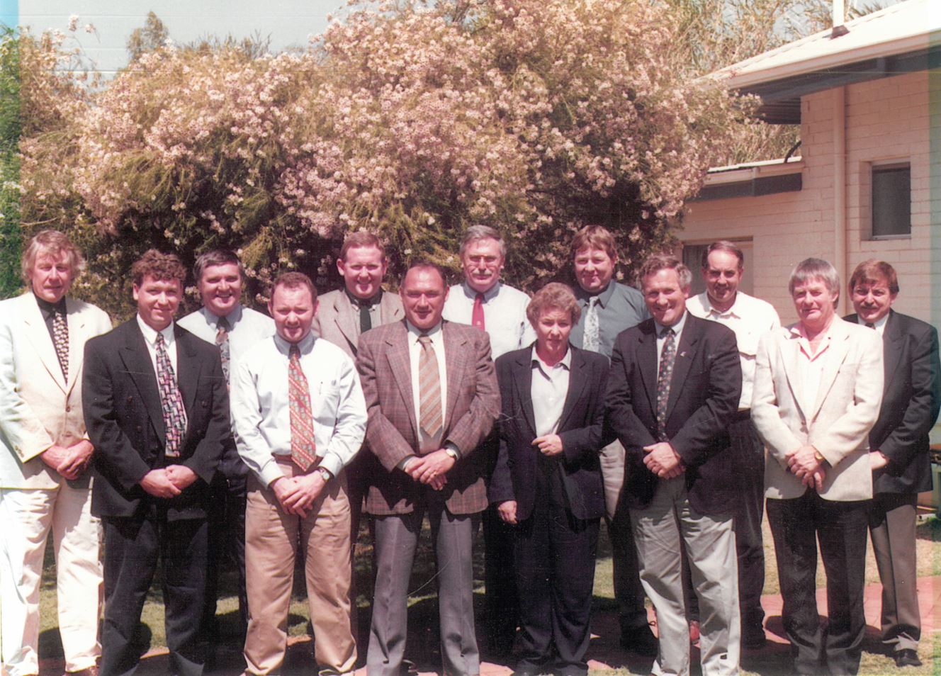 A group of men and women wearing suit and ties in a staff photo from 1990s