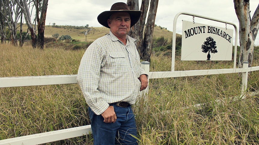 A farmer stands in front of his property gate
