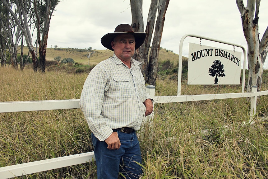 A farmer stands in front of his property gate