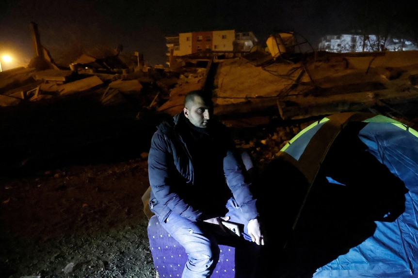 Mustafa Kazzaz sits beside a tent he now lives in after his apartment block collapsed