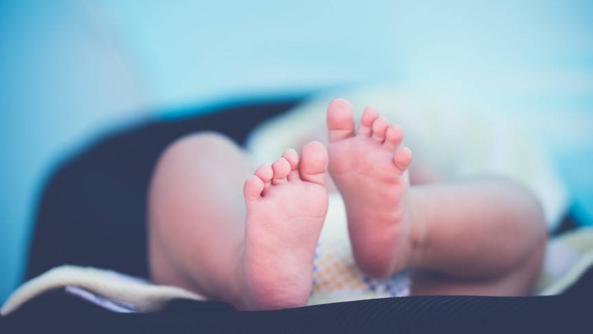 A blurred image of a newborn lying in blankets, with only the bottoms of their feet in focus.