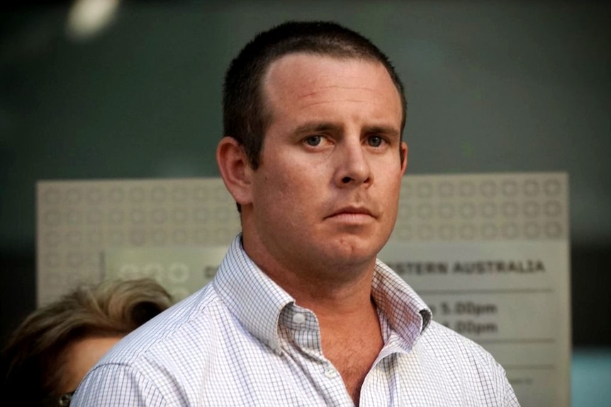 A close up photo of a man with short-cropped hair wearing an open shirt standing outside a court.