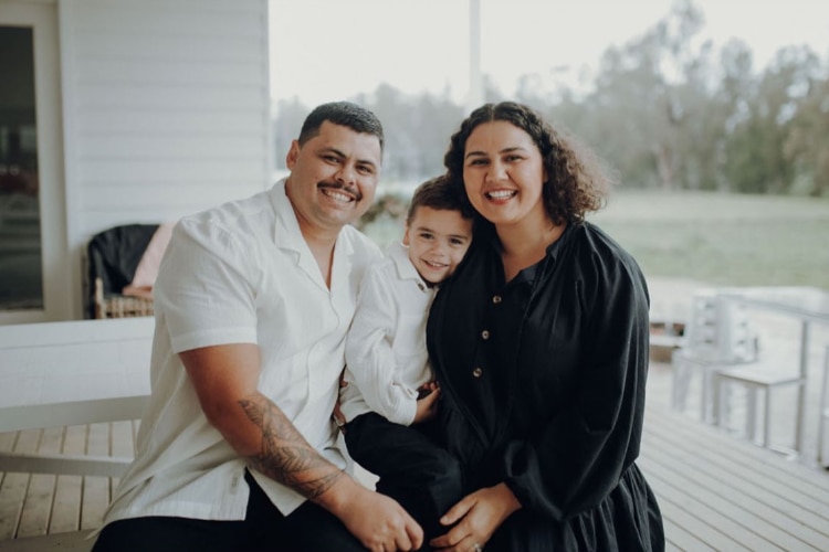 Father, son and mother sit together and smile while sitting on a backyard verander 