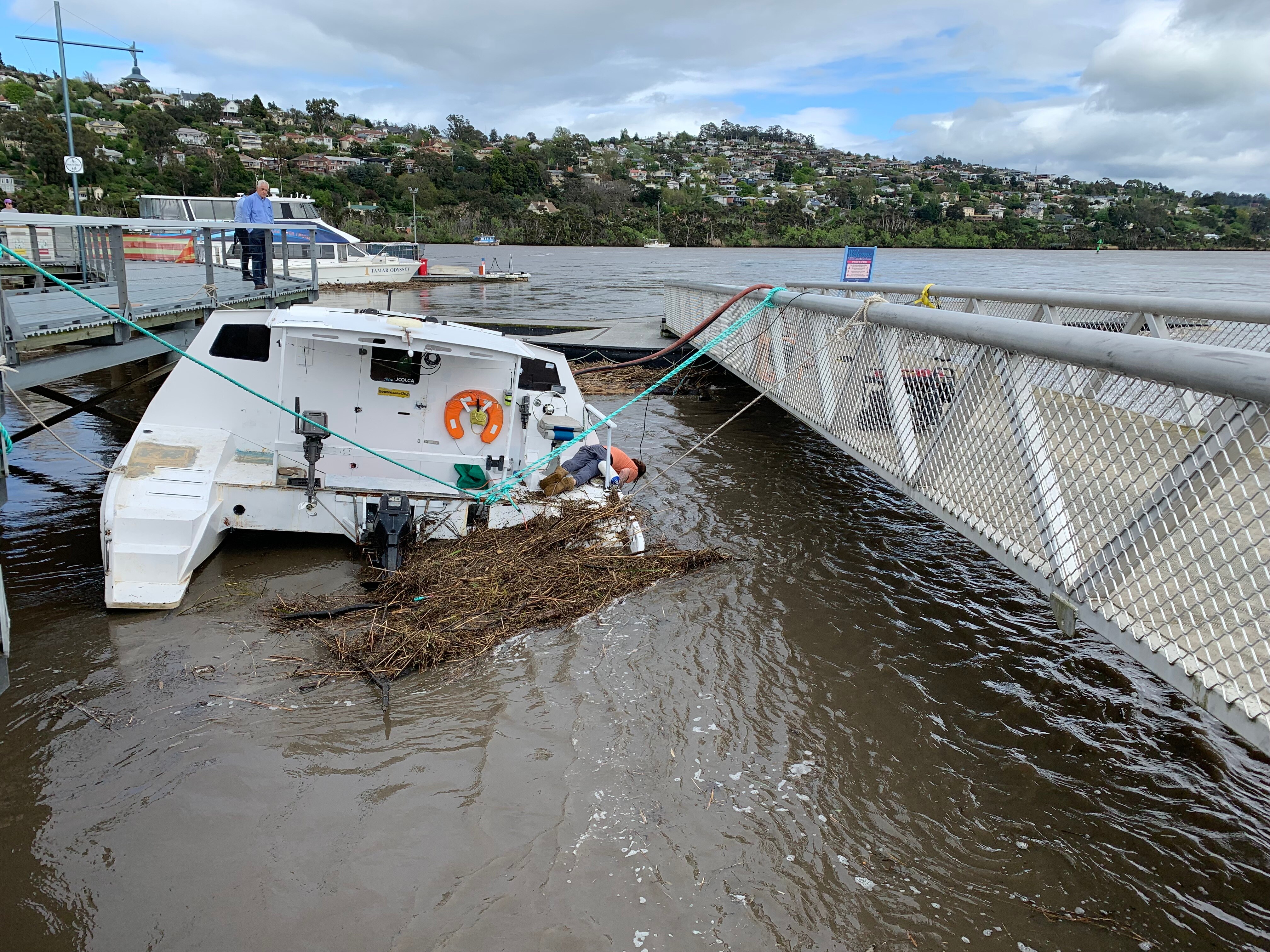 A boat is seen half-submerged in brown water next to a pontoon.