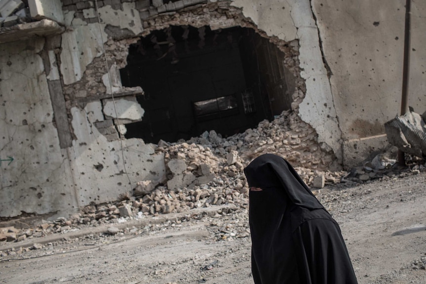 A woman wearing a niqab walks past a destroyed building in Mosul.