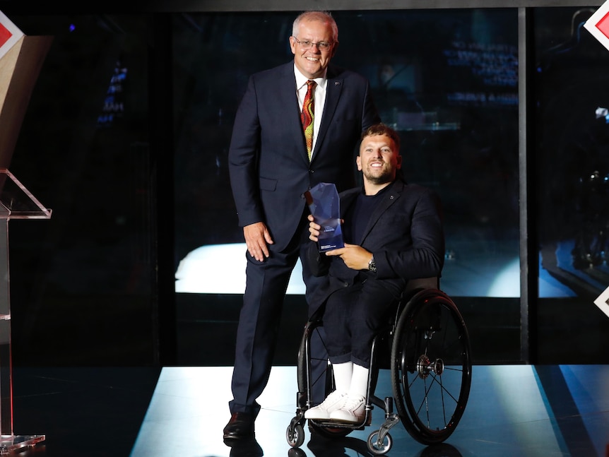 Dylan Alcott, in his wheelchair, accepts an award from Scott Morrison.