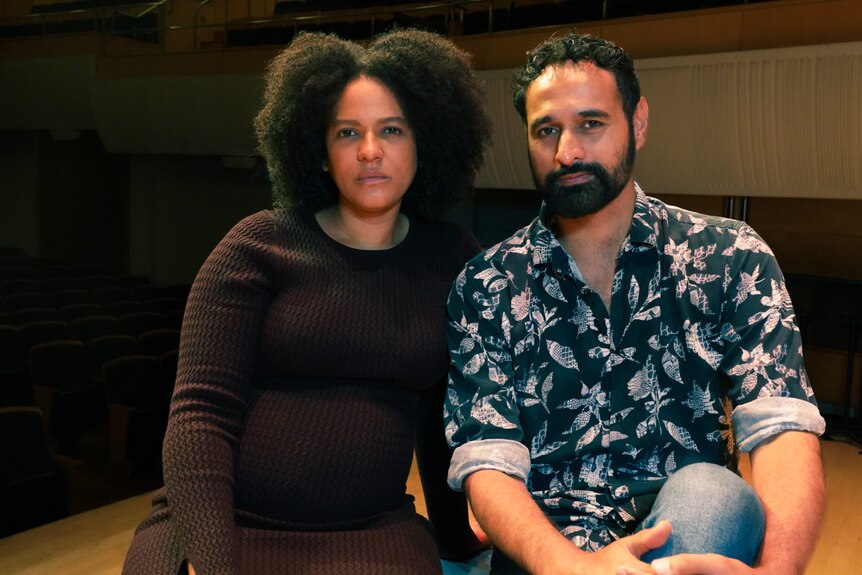Two actors, one woman with curly hair and one man with a beard and short black hair, look at the camera