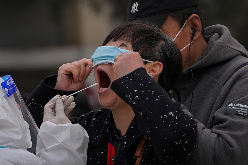 A woman pulls up her mask to get her throat swab 