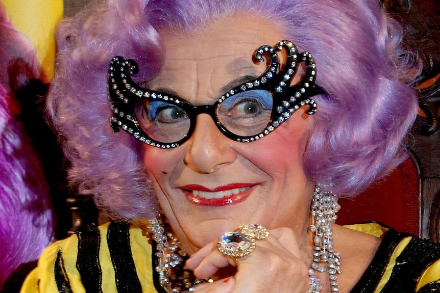 Barry Humphries as his alter ego Dame Edna, wearing a purple wig and extravagant glasses..