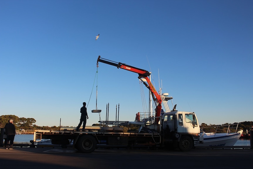 Community members use a small crane to load the concrete blocks onto the boat