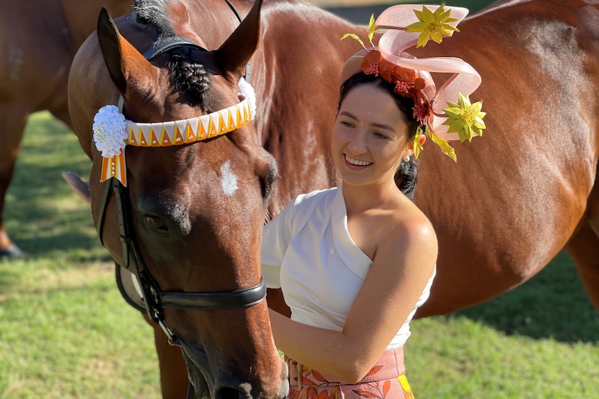 A smiling girl wearing fancy headwear holds a bay horse.