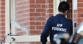 An AFP officer, with his back to the camera, outside the door of a brick building. His uniform says "AFP FORENSIC".