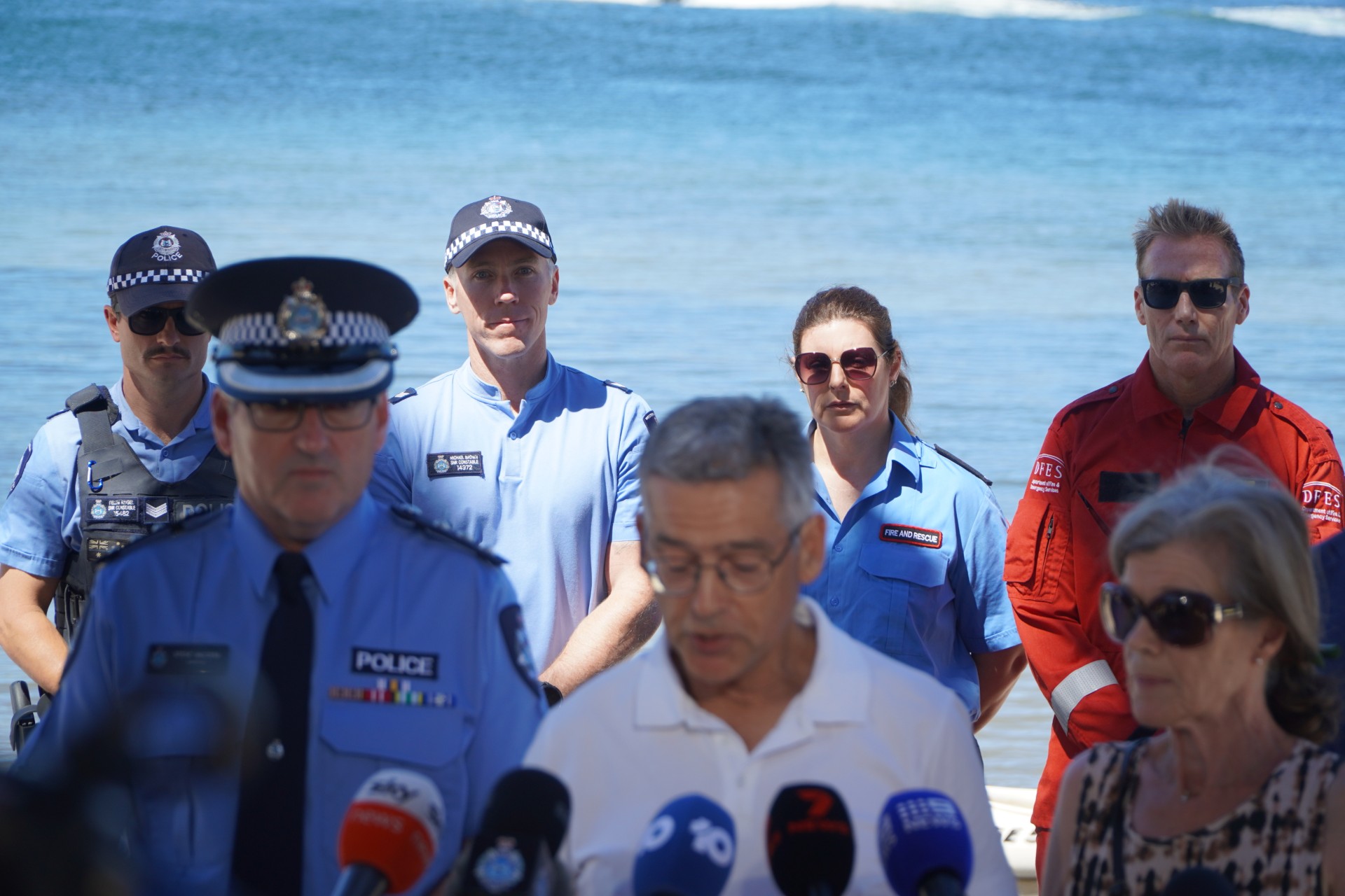 Um grupo de pessoas está à beira de um rio enquanto duas pessoas falam ao microfone.
