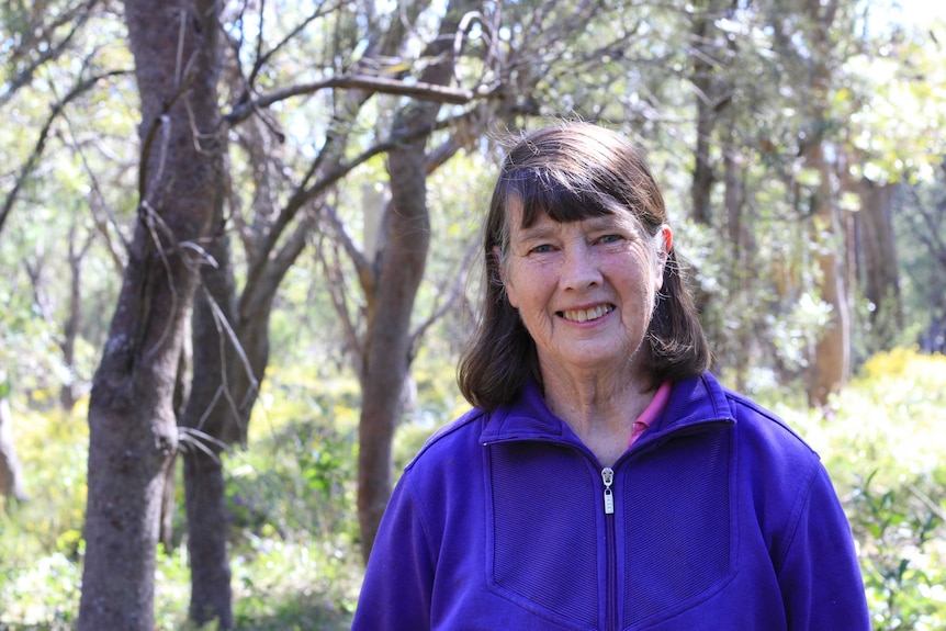 A woman with dark hair and a purple shirt stands outside