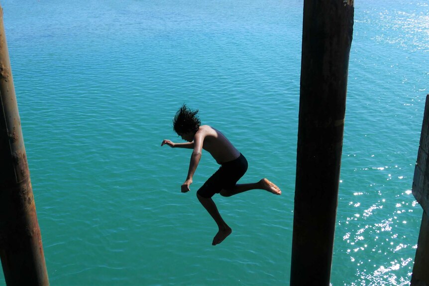 A boy jumps into the ocean off the Palm Island jetty