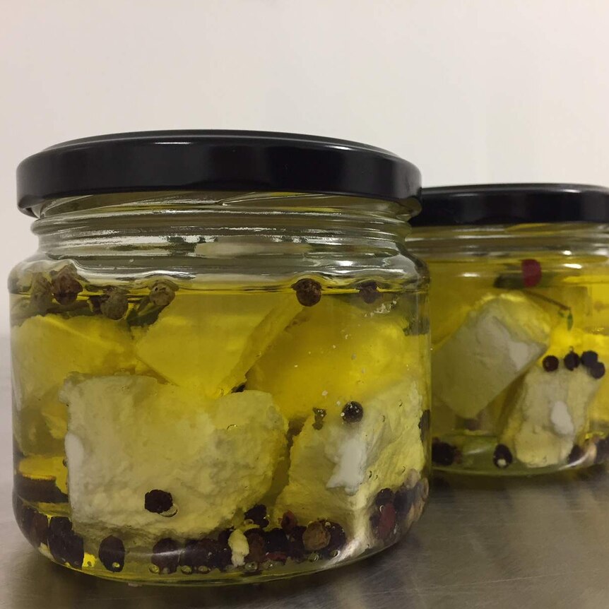 A close up of three jars filled with oil, feta cheese and peppercorns.