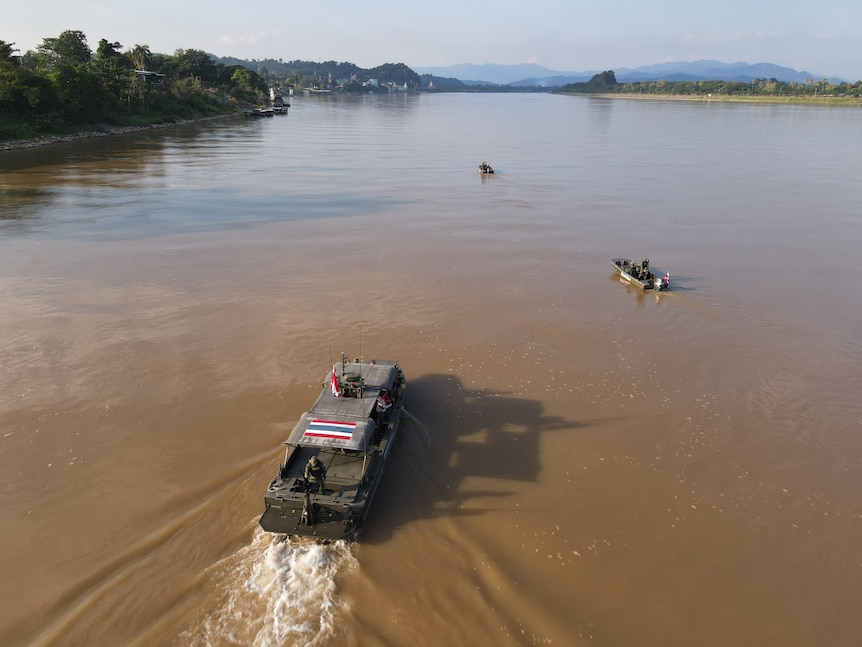 Aerial shot shows a larger patrolboat heading towards two smaller dinghies on a wide brown river