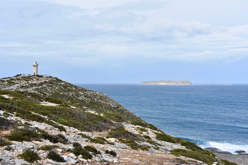 A lighthouse overlooks blue water and an island in the distance.