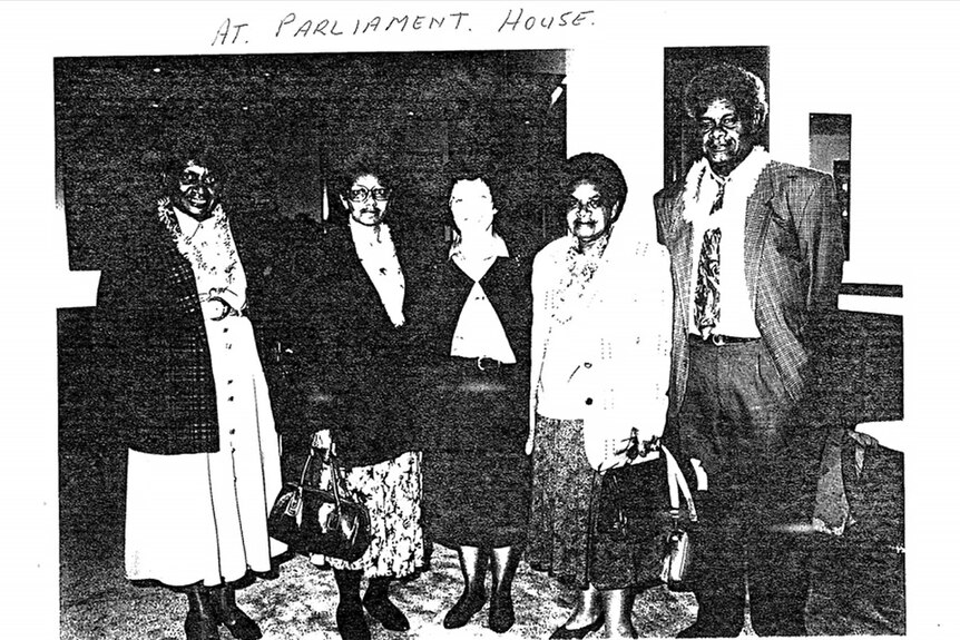 A scan of an old black and white photo with five people, including Aunty Doris, standing together smiling at parliament.