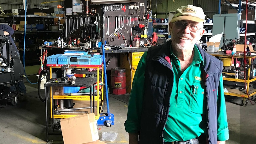 Garry Briggs stands in his workshop filled with tools and machinery.