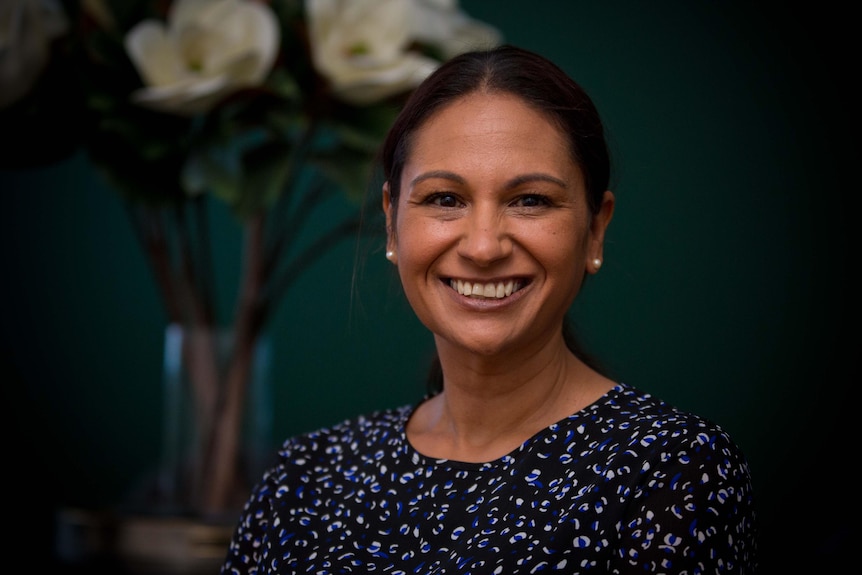 Belinda Wright looks at the camera in business attire in front of an arrangement of flowers.