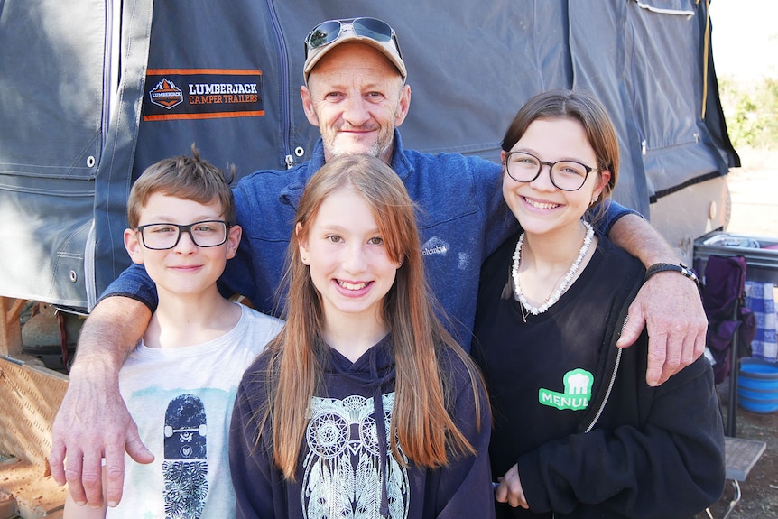 Victorian father Scott White stands with his three children next to a camper trailer at a caravan park.