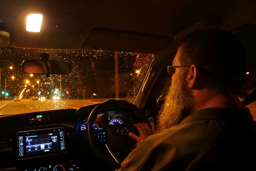 A photo of a man at the wheel of a vehicle at night.