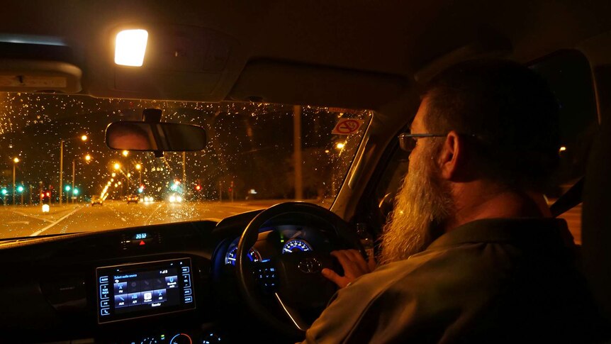 A photo of a man at the wheel of a vehicle at night.