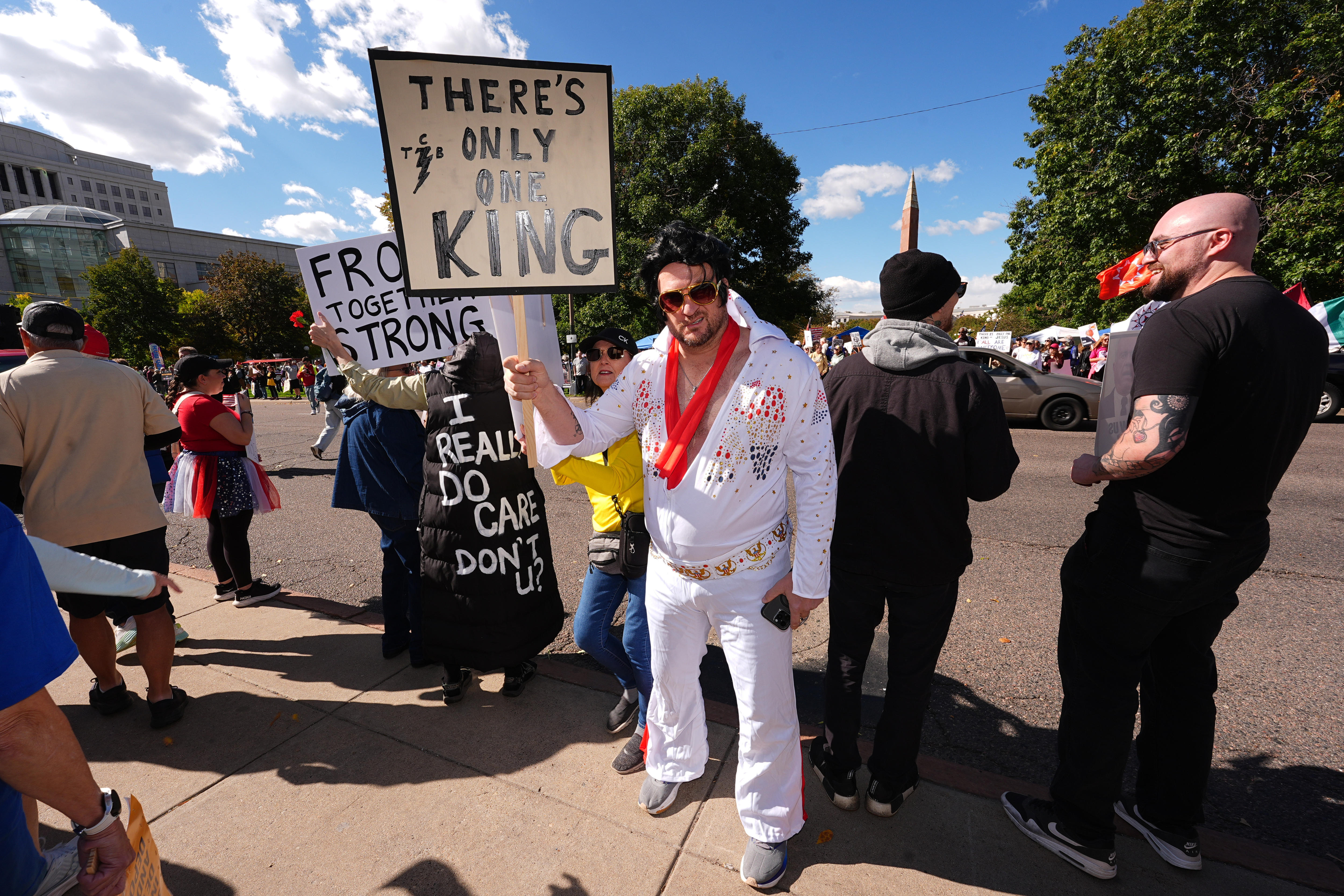 A protester in an Elvis Presley costume holding a sign with a 'There's Only One King' message