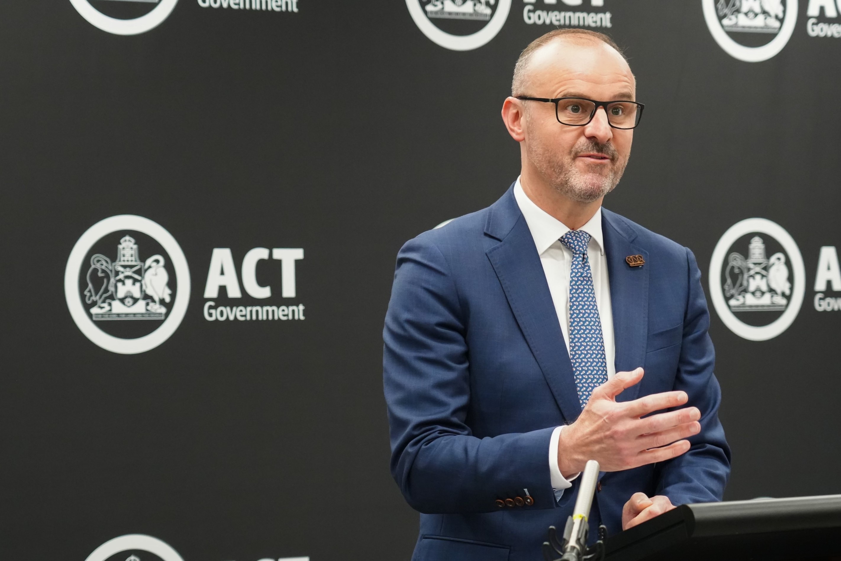 A man in a navy suit speaks at a lectern.