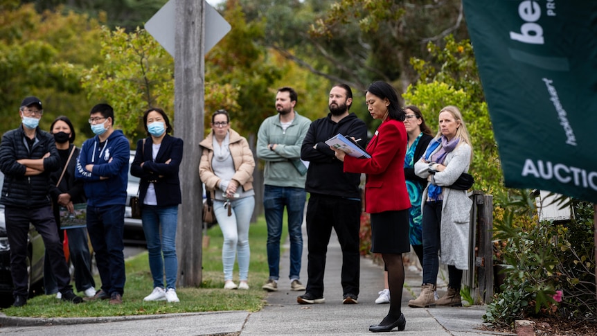 a woman taking notes while another group of people look on while a property auction is underway