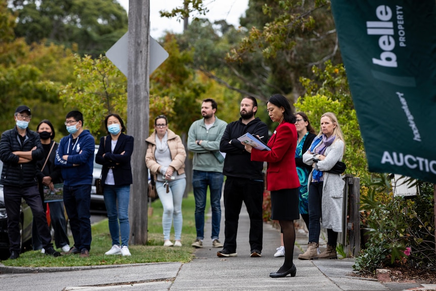 a woman taking notes while another group of people look on while a property auction is underway